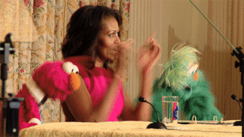 Michelle Obama does a happy dance with two muppets.